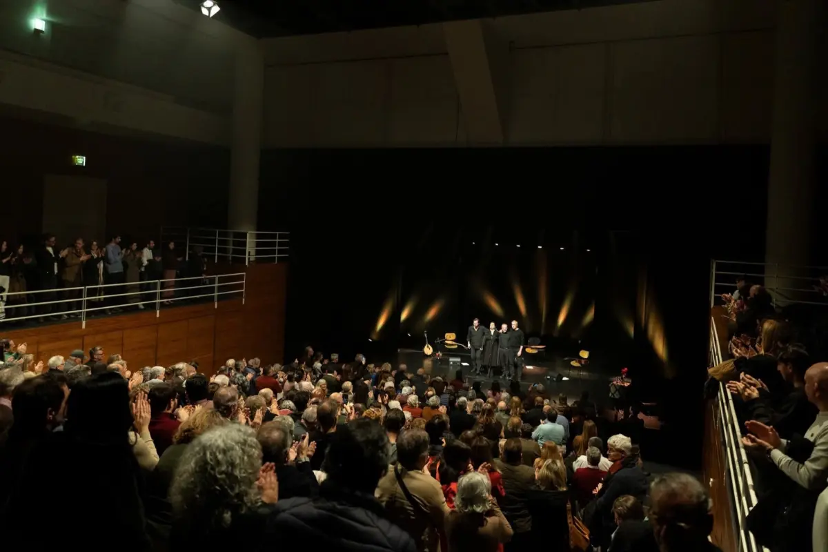 Audiência em pé a aplaudir, palco com luzes laranjas.